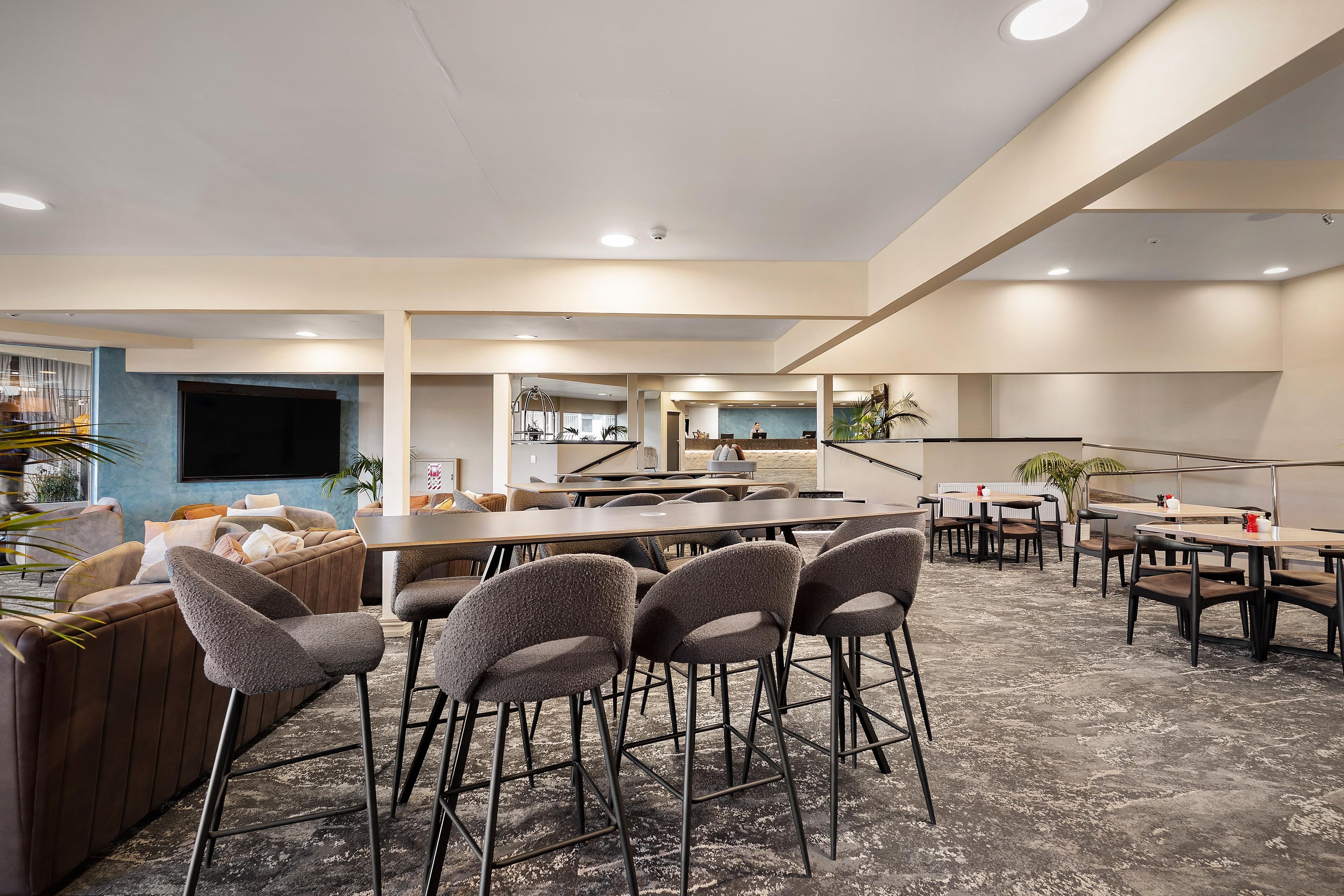 A spacious hotel lobby with a bar area, seating arrangements, and a reception desk.