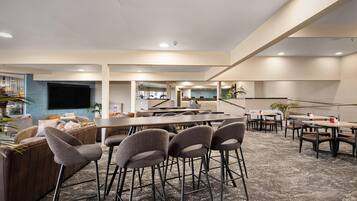 A spacious hotel lobby with a bar area, seating arrangements, and a reception desk.