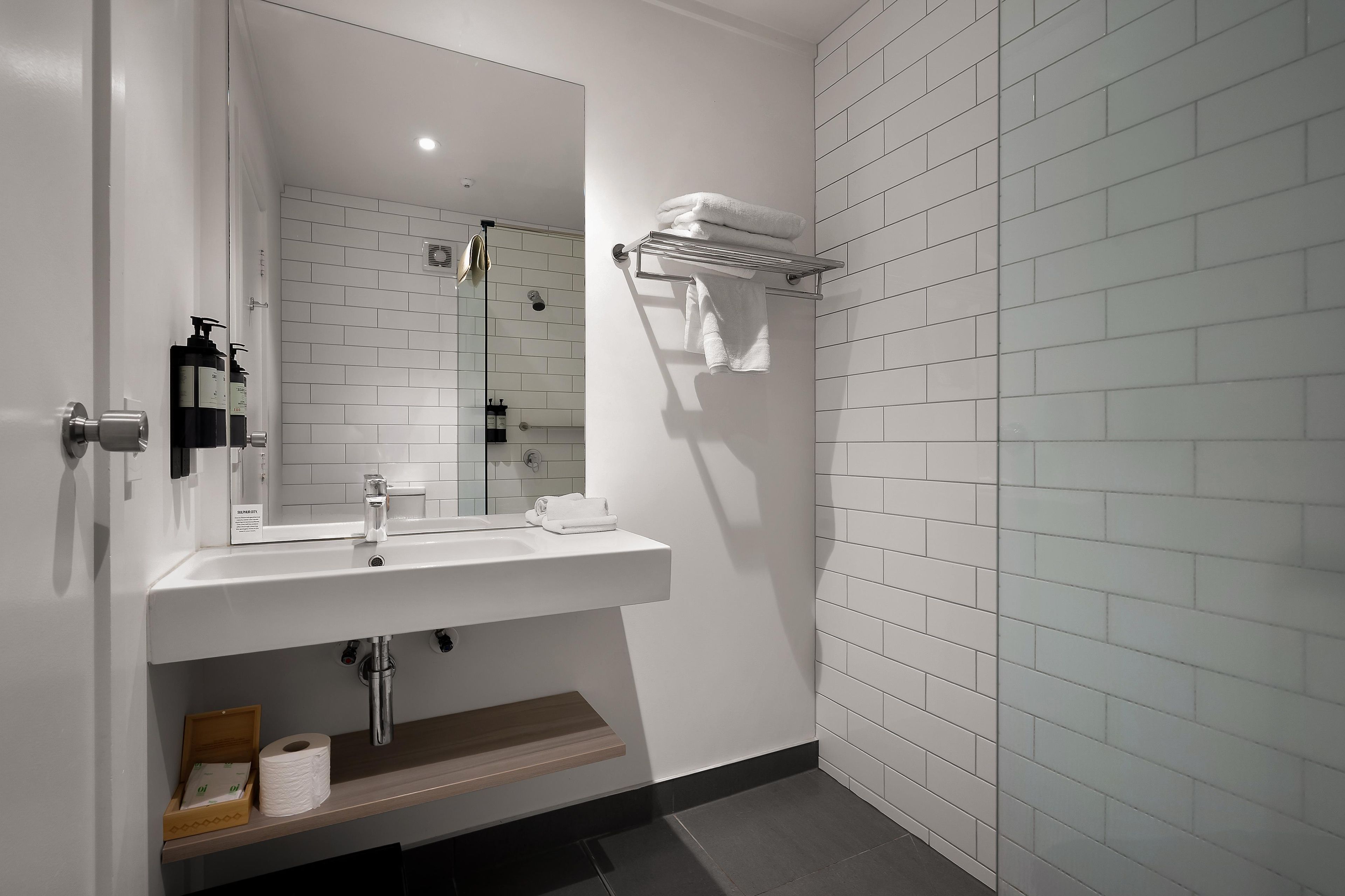 A modern bathroom with a white sink, mirror, and towel rack.