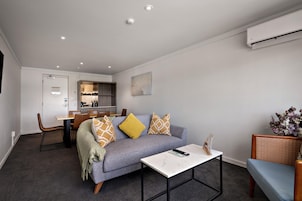Una sala de estar moderna con un sofá gris, una mesa de centro y un comedor con sillas y una encimera de cocina.