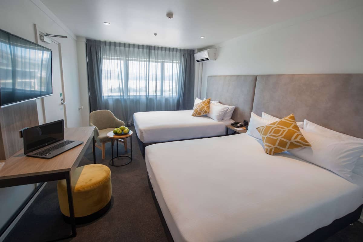 A hotel room with two beds, a desk with a laptop, a chair, and a small table with fruit.