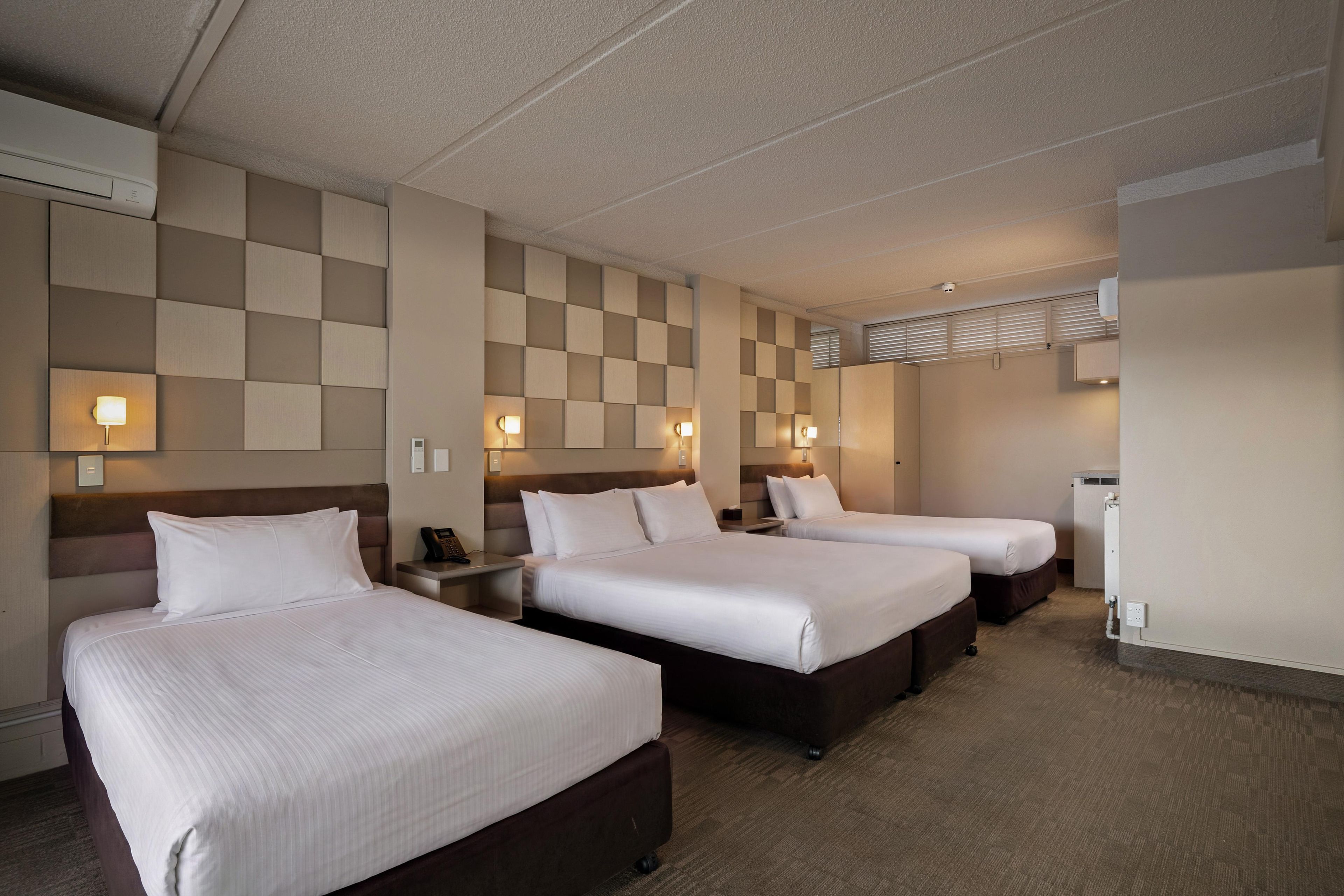A hotel room with three beds, a minibar, and a wall-mounted air conditioning unit.