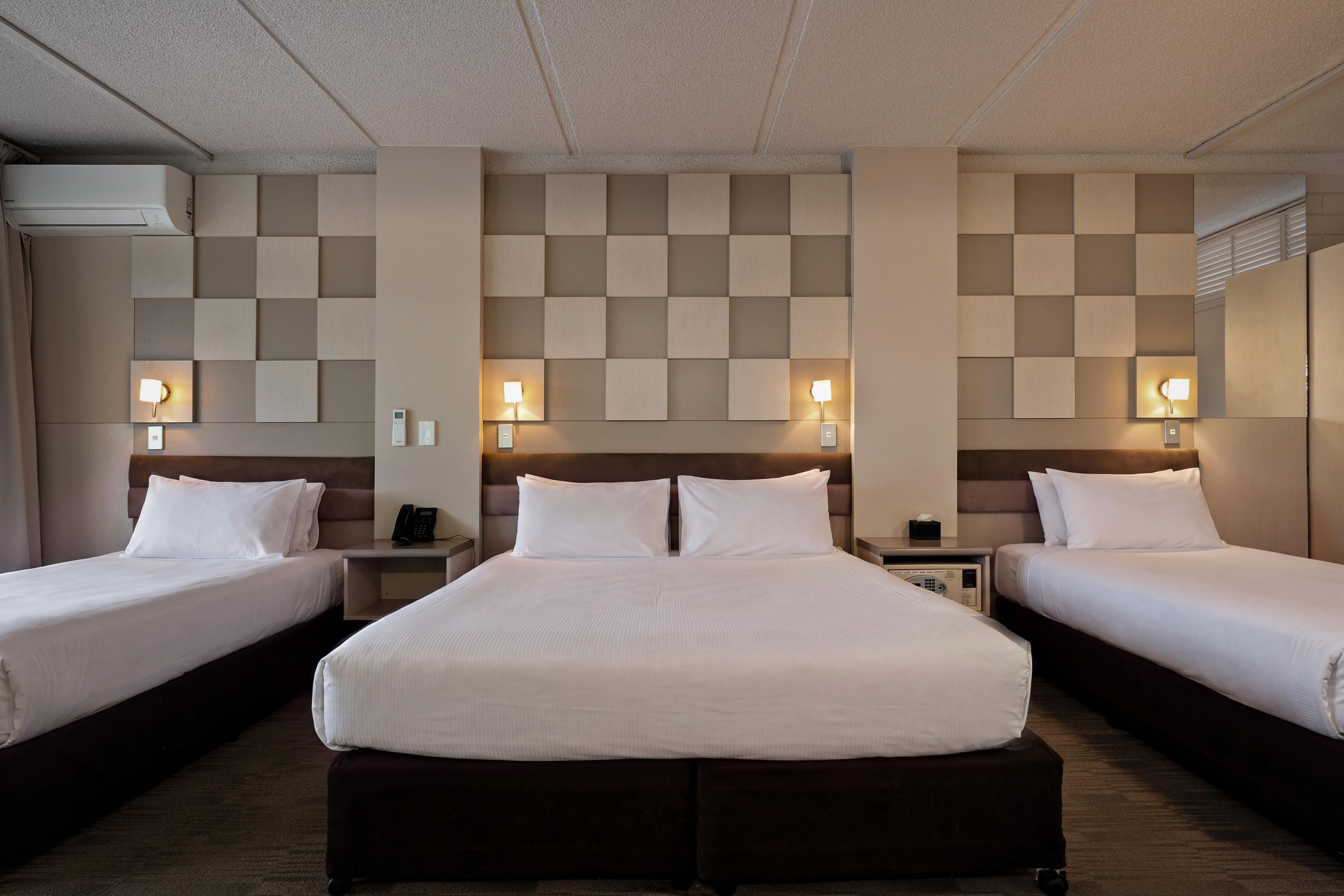 A hotel room with two single beds, a large bed, and a headboard with a built-in phone.
