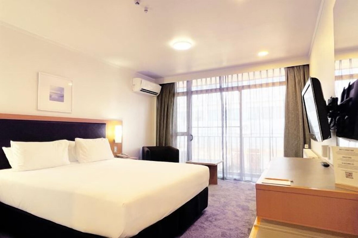 Een hotelkamer met een groot bed, een bureau, een stoel en een raam met gordijnen.