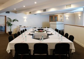 Un salón de conferencias con una larga mesa, sillas, botellas de agua y un reloj en la pared.