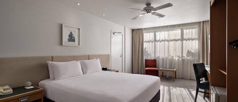 Ein Hotelzimmer mit Bett, Nachttisch, Stuhl, Schreibtisch und Deckenventilator.