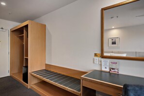 Une pièce comprenant une armoire en bois, un bureau avec une chaise, un miroir et une petite étagère.
