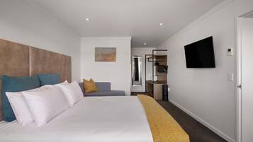 Quarto de hotel moderno com cama grande, sofá, televisão e espelho.