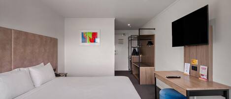 Habitació d'hotel amb un llit, una taula de treball, una cadira, una televisió i una petita obra d'art a la paret.