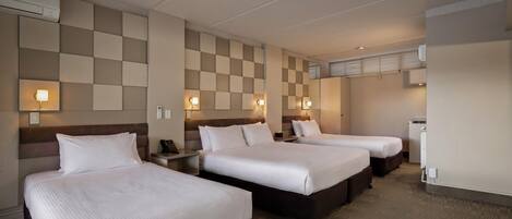 A hotel room with three beds, a minibar, and a wall-mounted air conditioning unit.