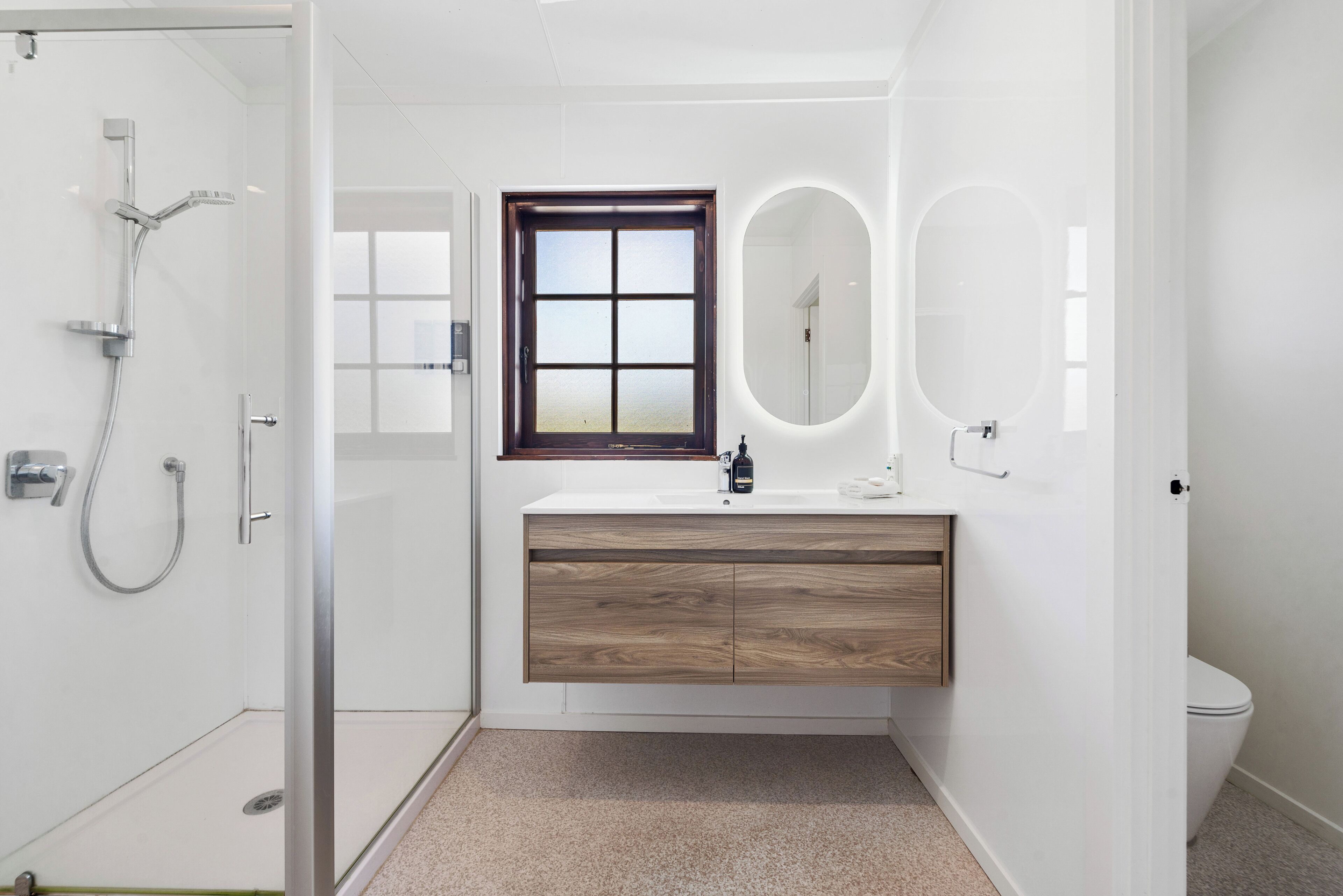 Un baño moderno con cabina de ducha de vidrio, tocador de madera con espejo y un inodoro.