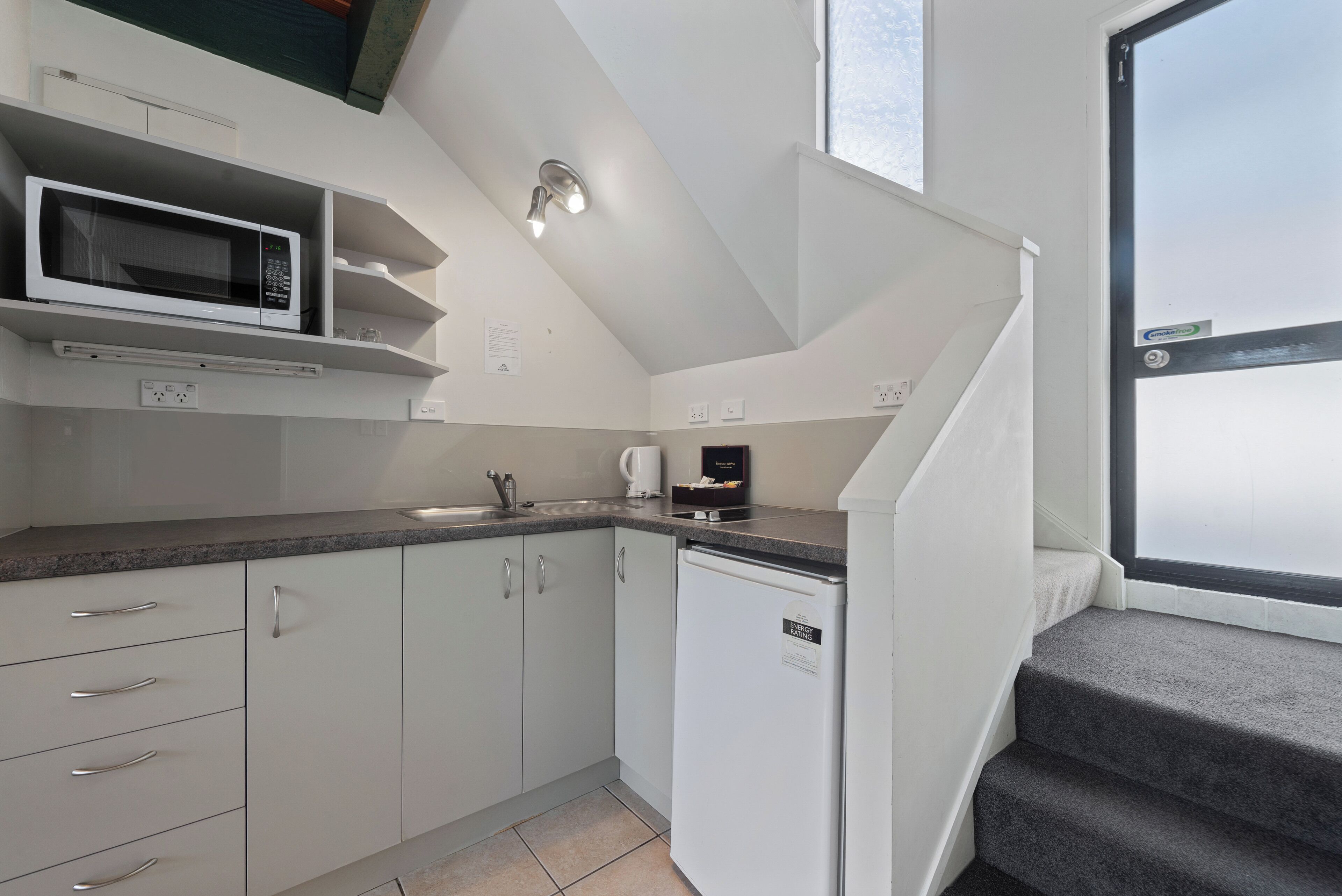A compact kitchen with white cabinets, a microwave, a coffee maker, and a dishwasher.