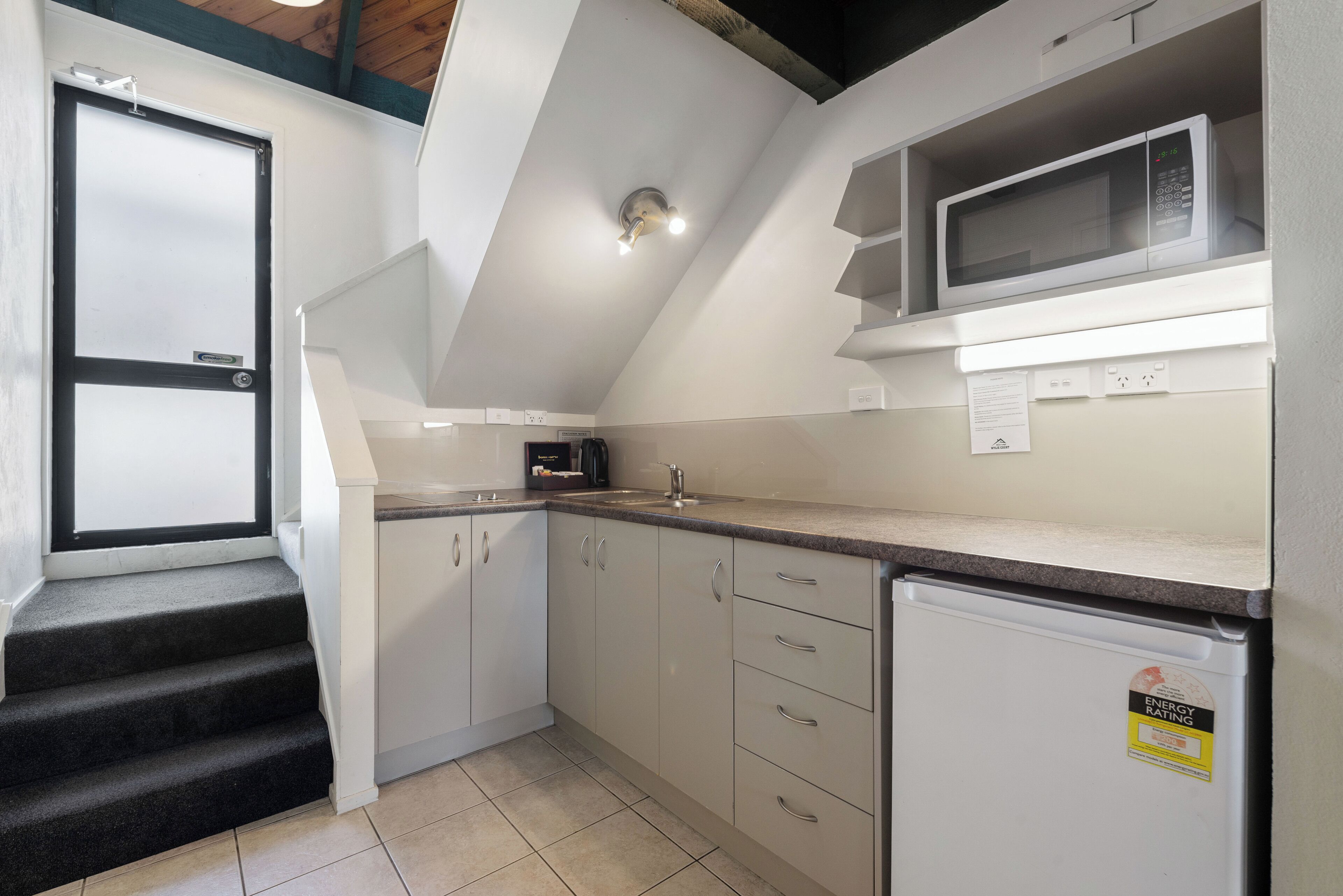A kitchen with a microwave, refrigerator, and a sink. There are cabinets and a countertop.