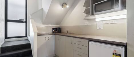 A kitchen with a microwave, refrigerator, and a sink. There are cabinets and a countertop.
