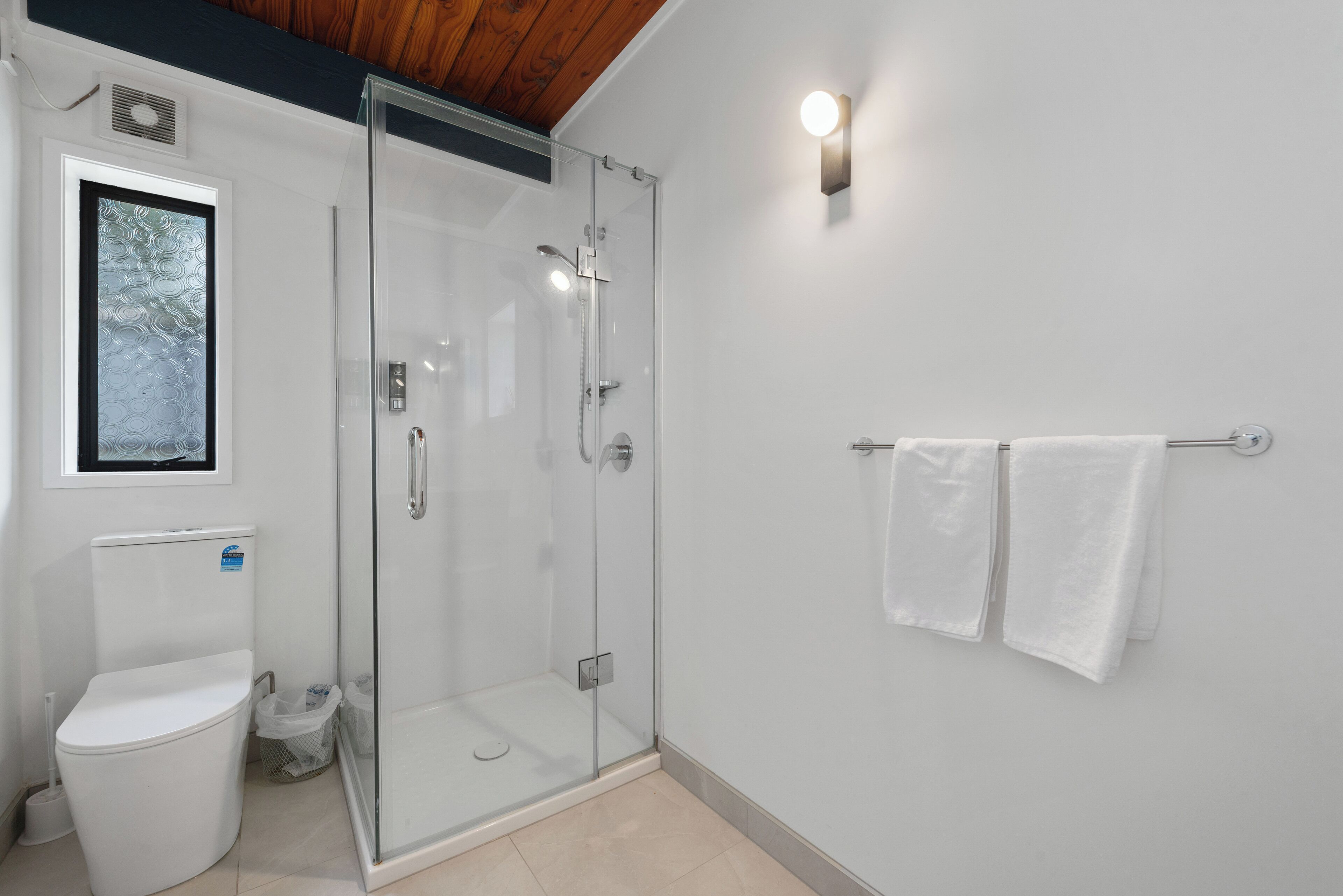 A modern bathroom with a glass-enclosed shower, a toilet, and a towel rack.