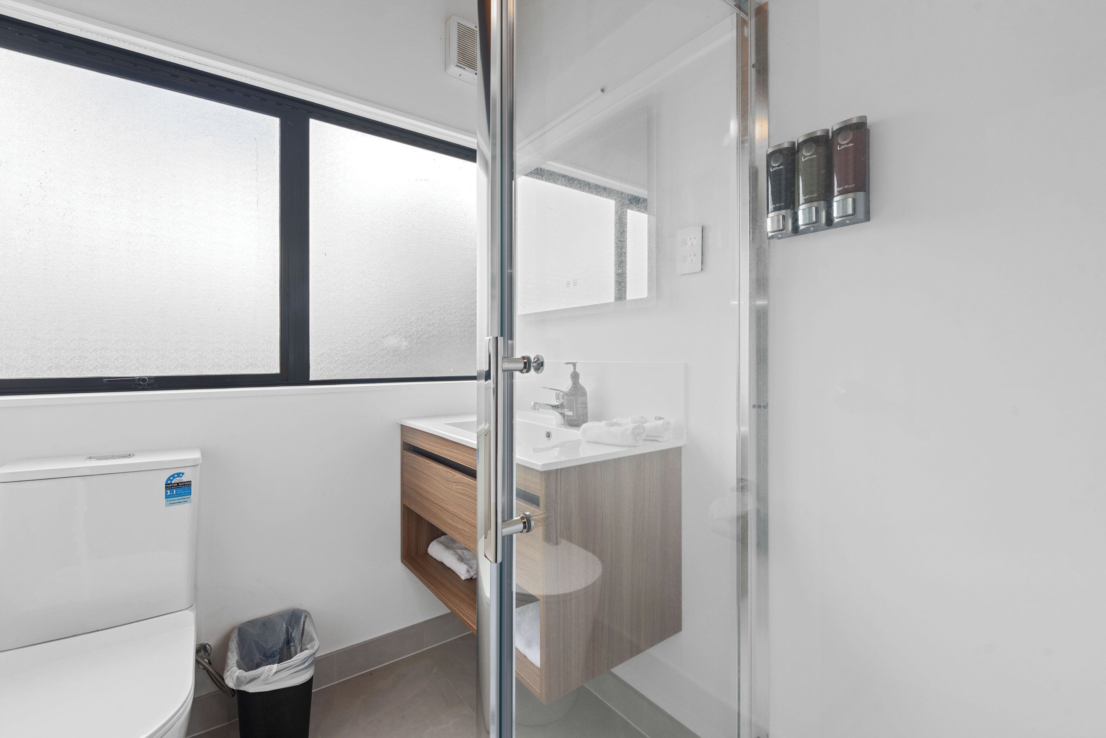 Un baño moderno con cabina de ducha de vidrio, tocador de madera y lavamanos blanco.