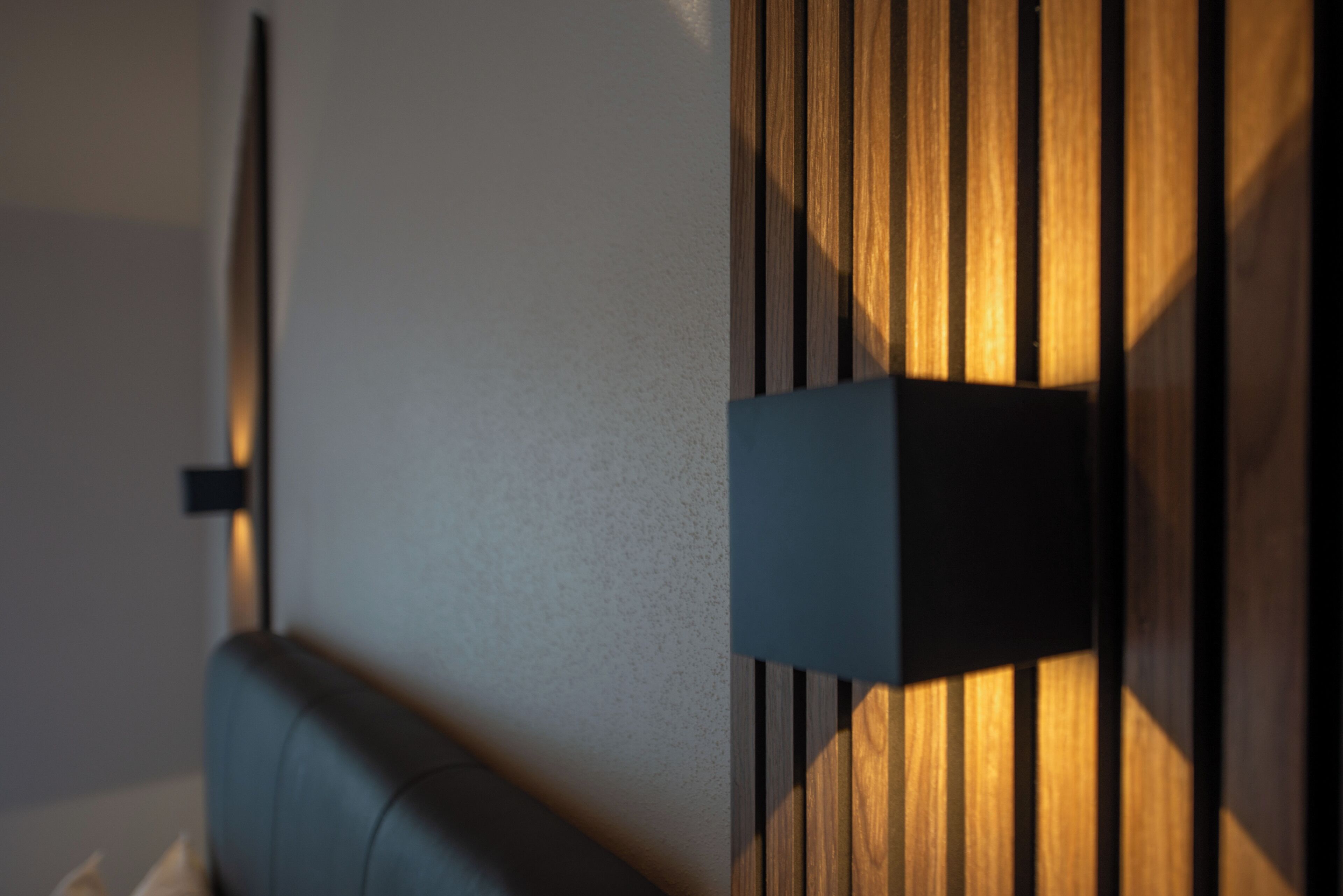 Pared moderna con listones verticales de madera y una lámpara horizontal.
