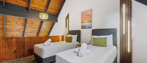 Une chambre d’hôtel avec deux lits, des poutres apparentes en bois au plafond, un tableau et un luminaire moderne.