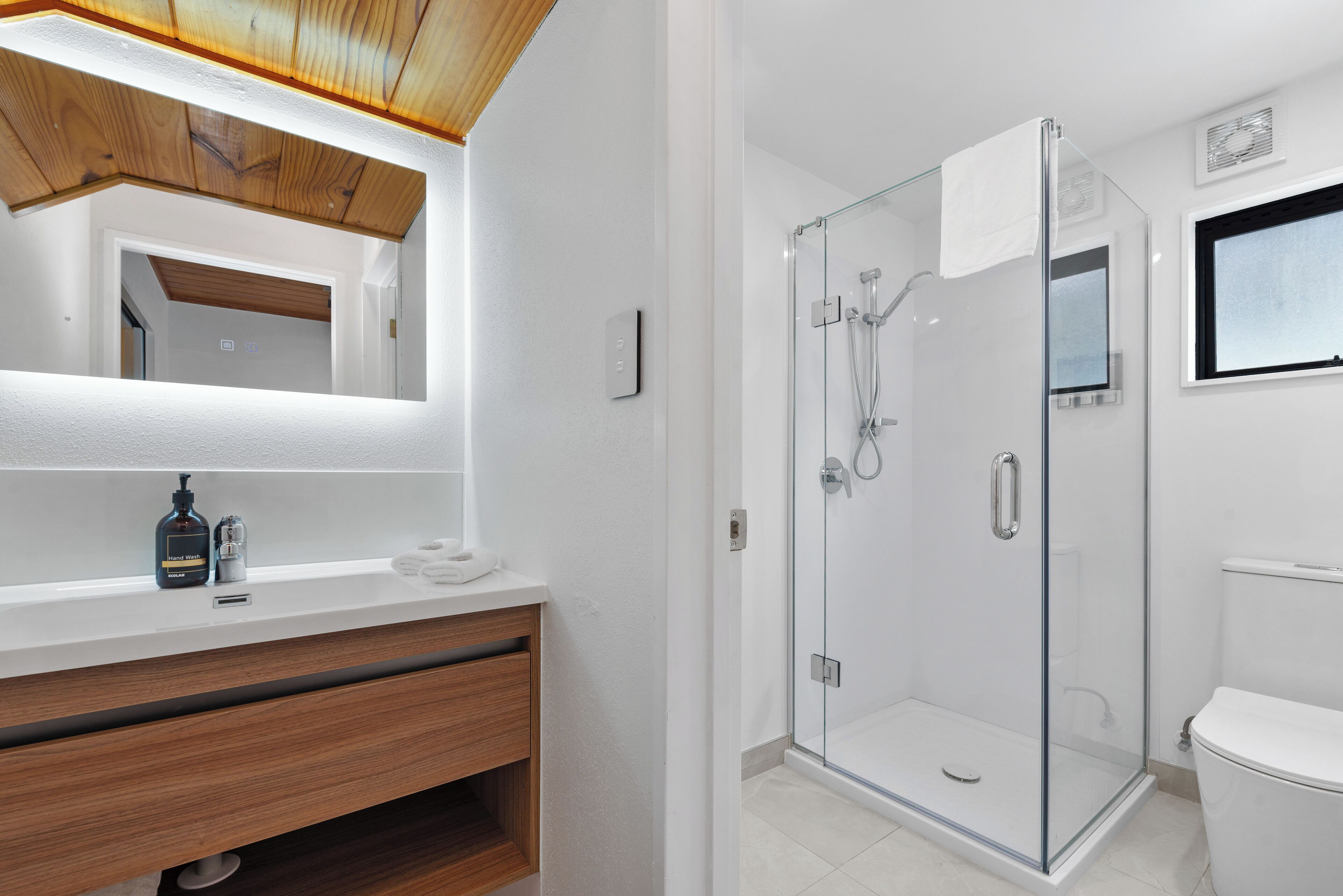 A modern bathroom with a wooden ceiling, a glass shower enclosure, and a white toilet.