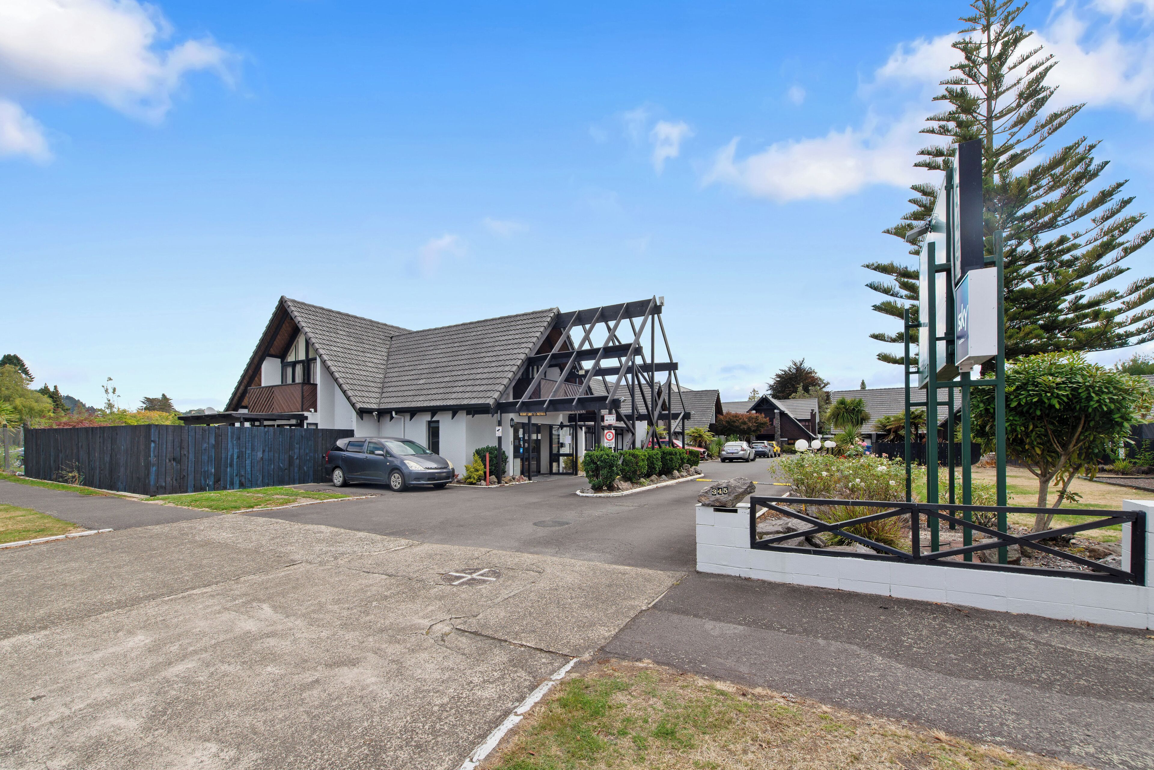 A modern building with a sloped roof, a fenced driveway, and a parking area.
