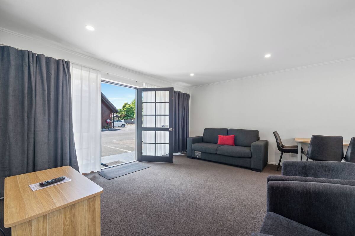 A modern hotel room with a grey sofa, a small wooden table, and a grey armchair.