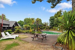 A backyard with a pool, lounge chairs, a picnic table, and various plants.