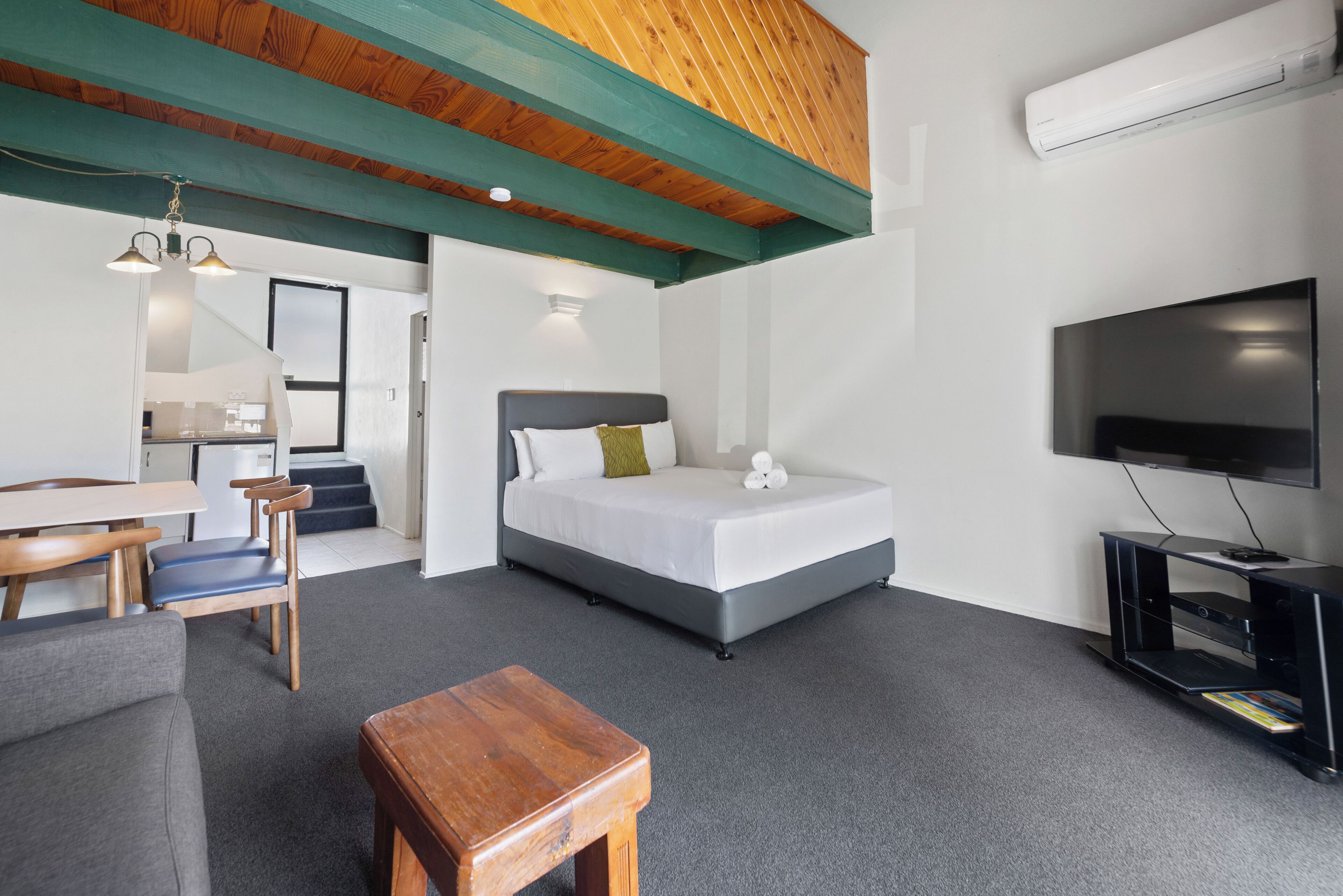 A modern hotel room with a bed, a desk, a chair, a TV, and a staircase leading to another room.