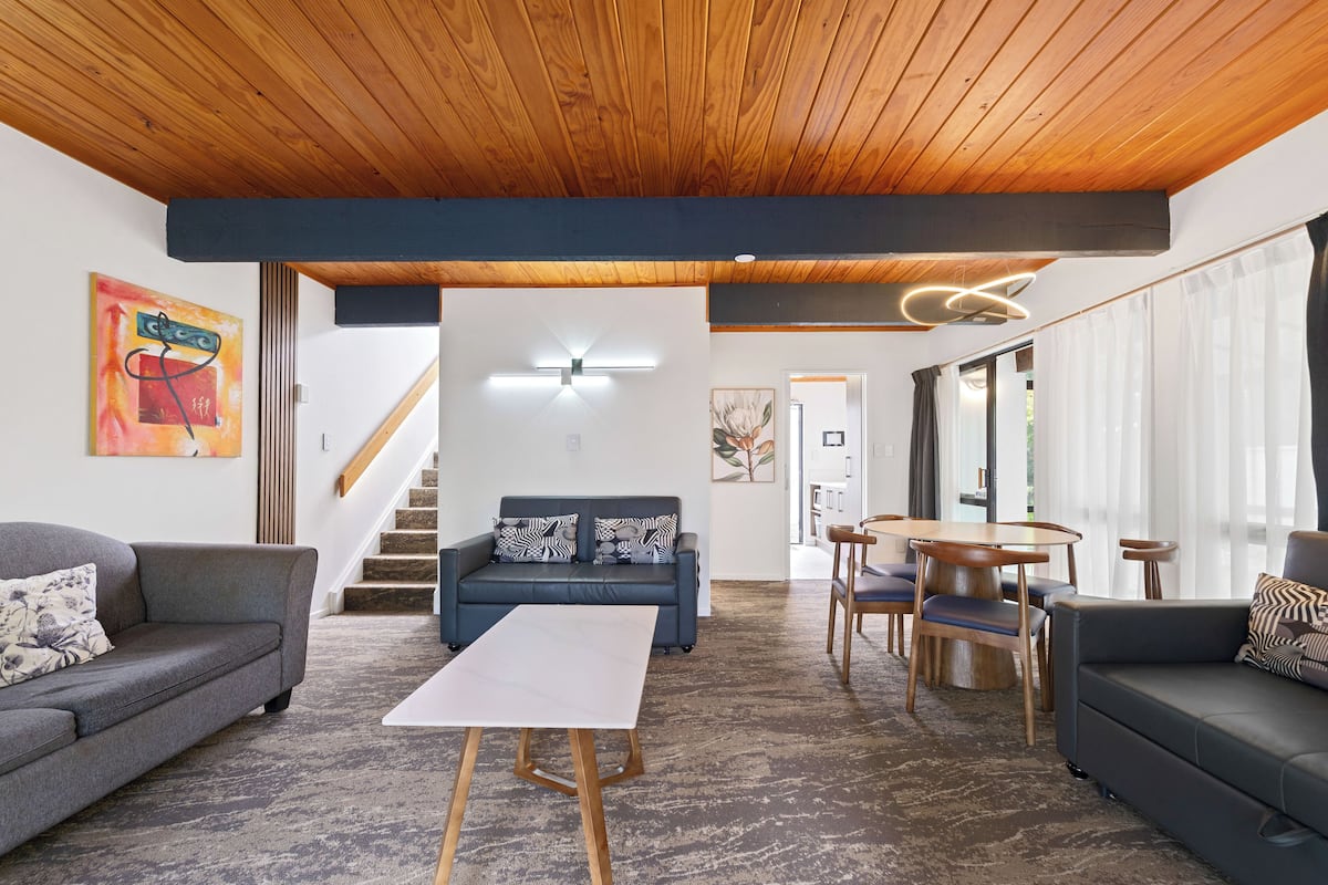 A modern living room with a wooden ceiling, a sofa, a coffee table, and a dining area with chairs and a table.