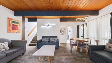 A modern living room with a wooden ceiling, a sofa, a coffee table, and a dining area with chairs and a table.