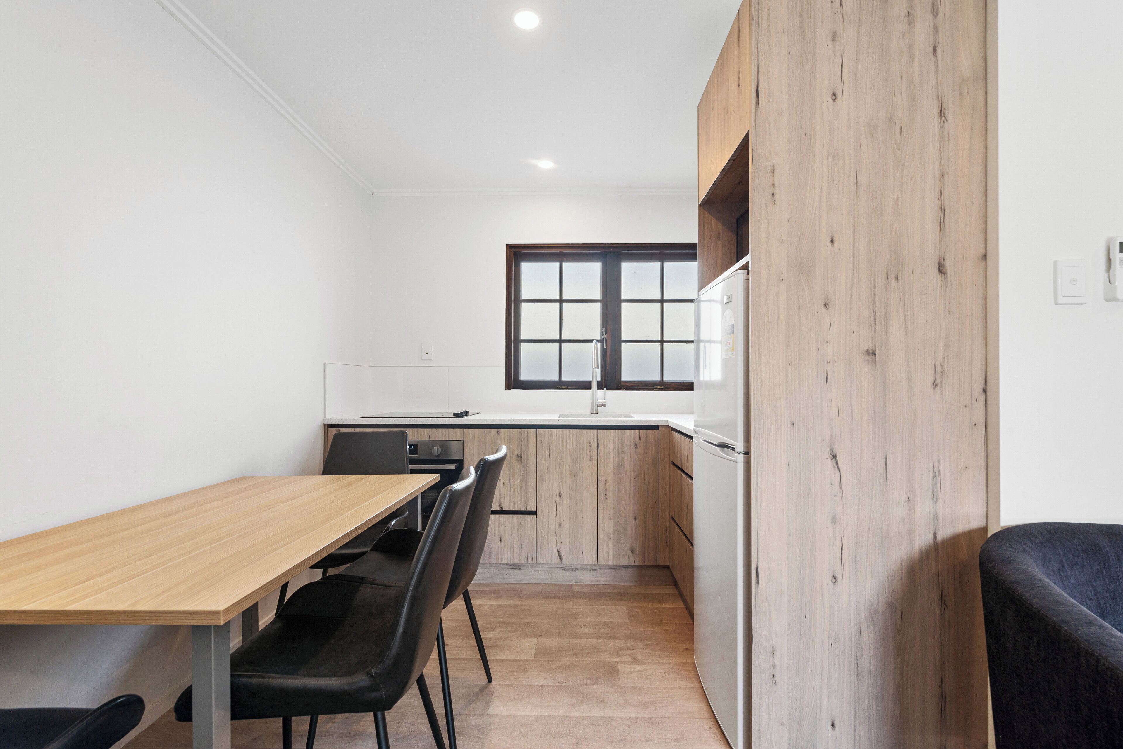 A compact kitchen with a wooden table, black chairs, and a window.