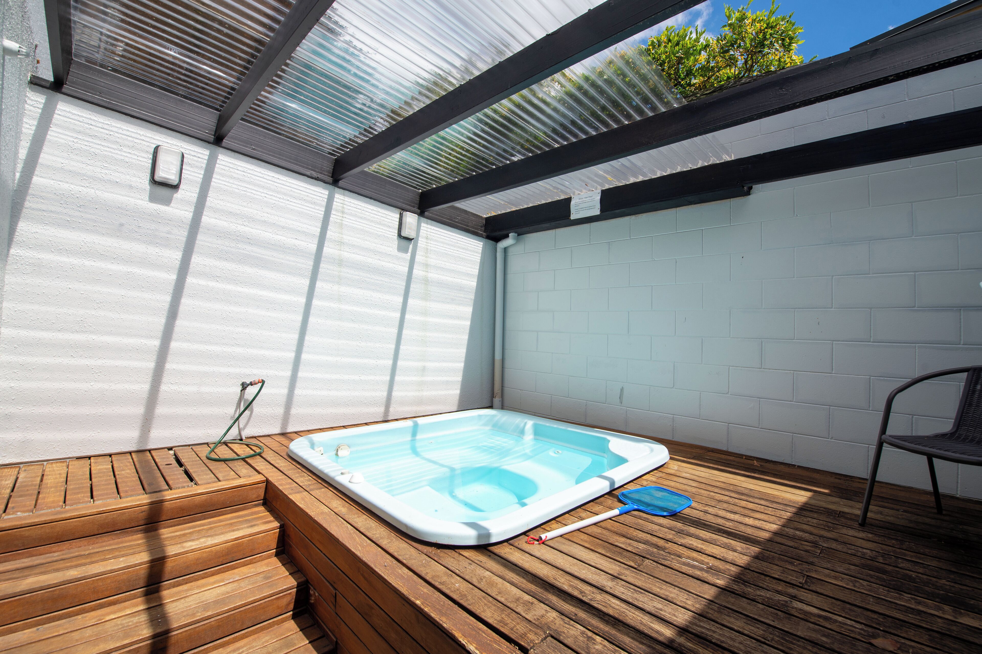 Un bain à remous situé dans un espace extérieur abrité, doté d’une terrasse en bois et d’un toit en métal.