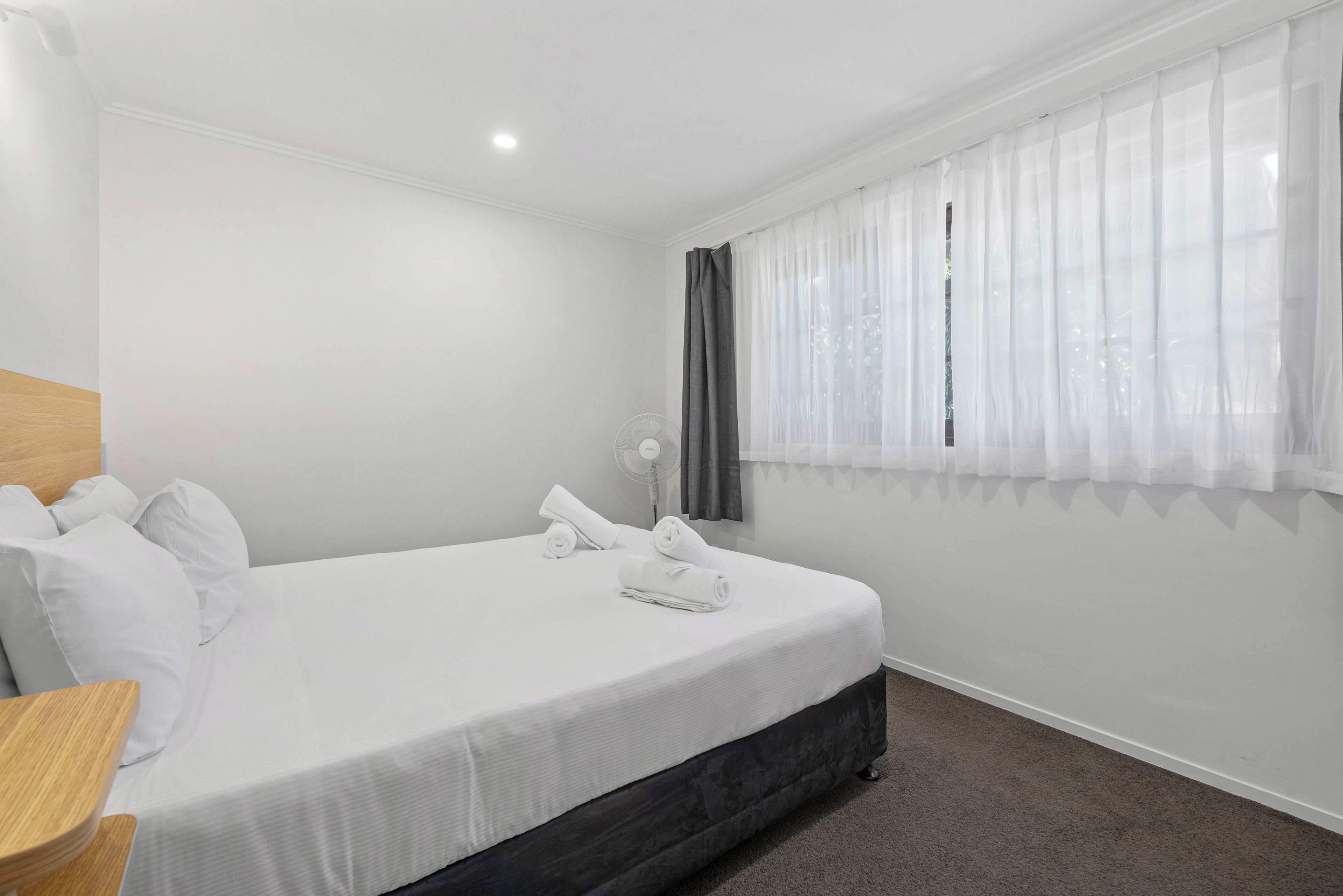 A neatly made bed with white linens, a wooden nightstand, and a bedside table.