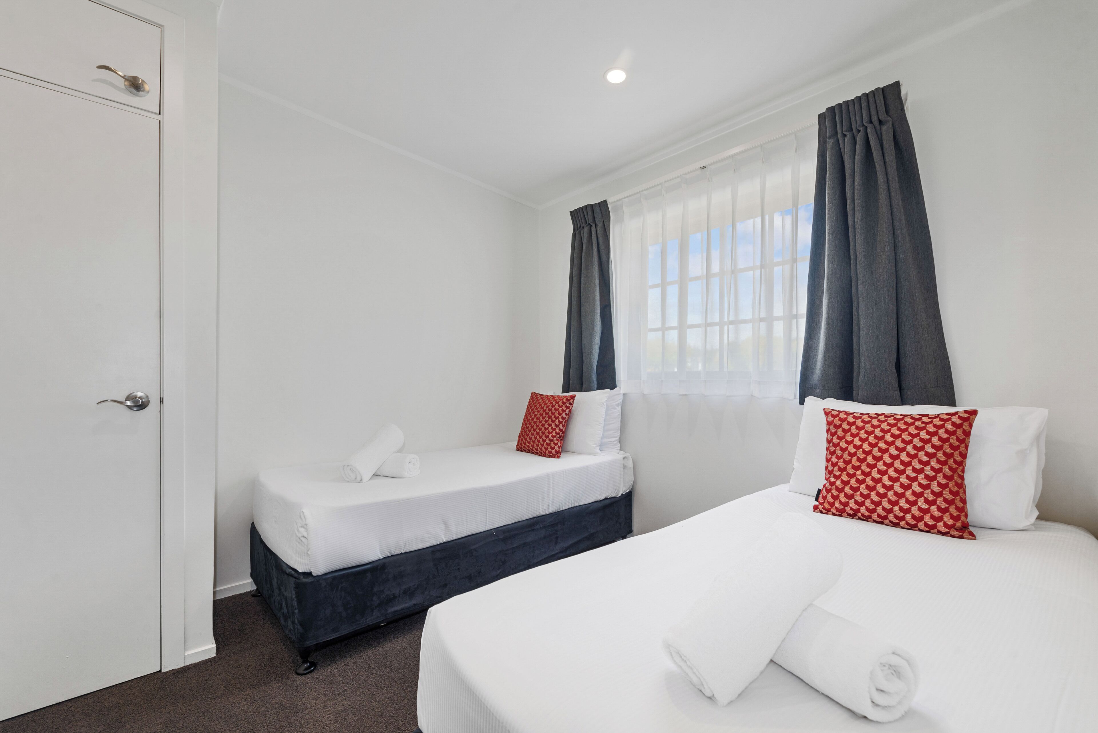 Una habitación de hotel con dos camas, una puerta blanca y un ventanal con cortinas.