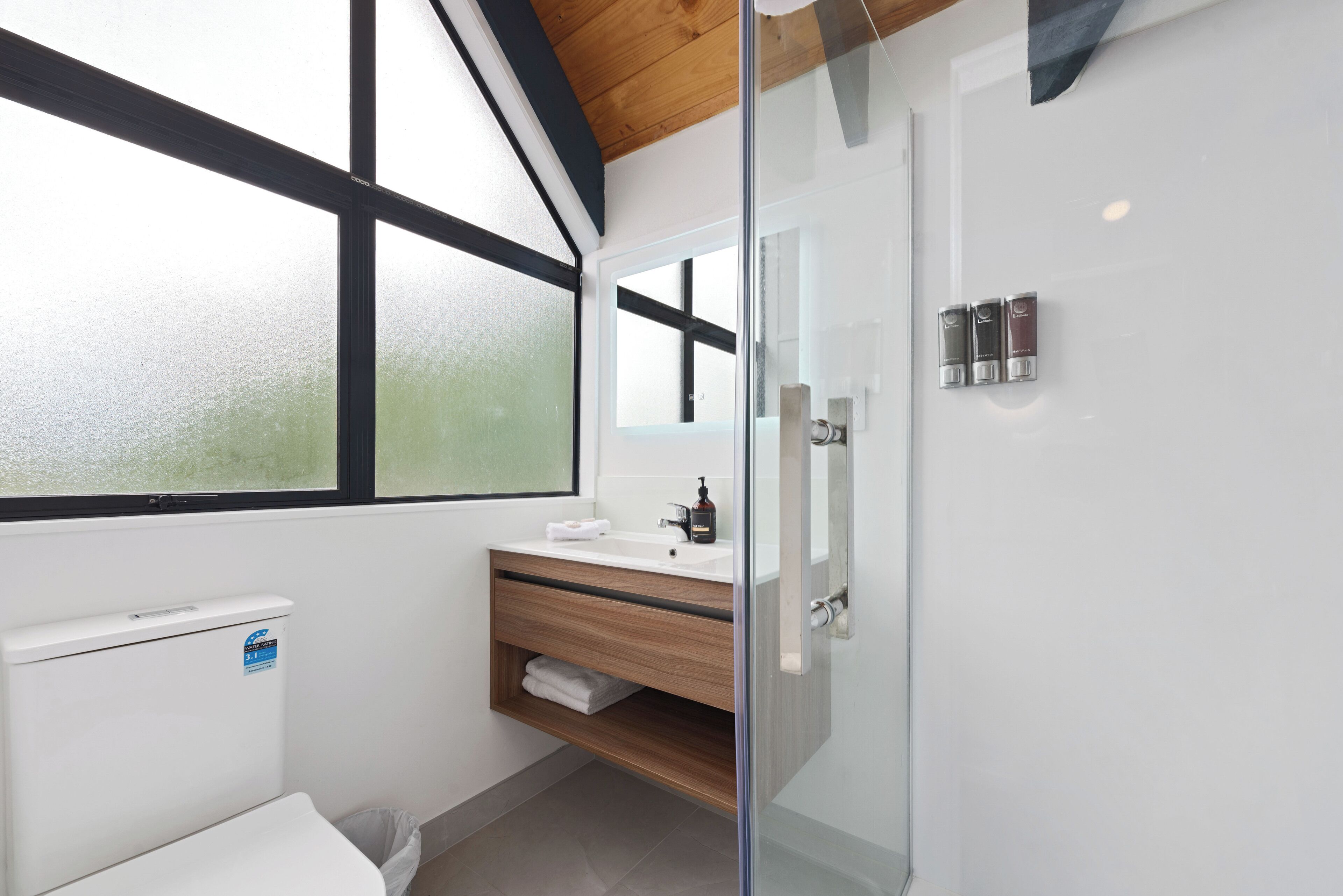 A modern bathroom with a glass shower enclosure, a white sink with a wooden vanity, and a window providing natural light.