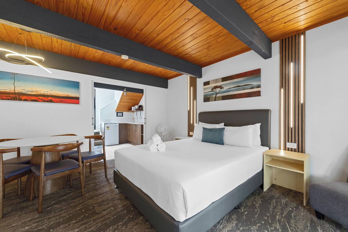 A hotel room with a large bed, a desk with chairs, and artwork on the walls.