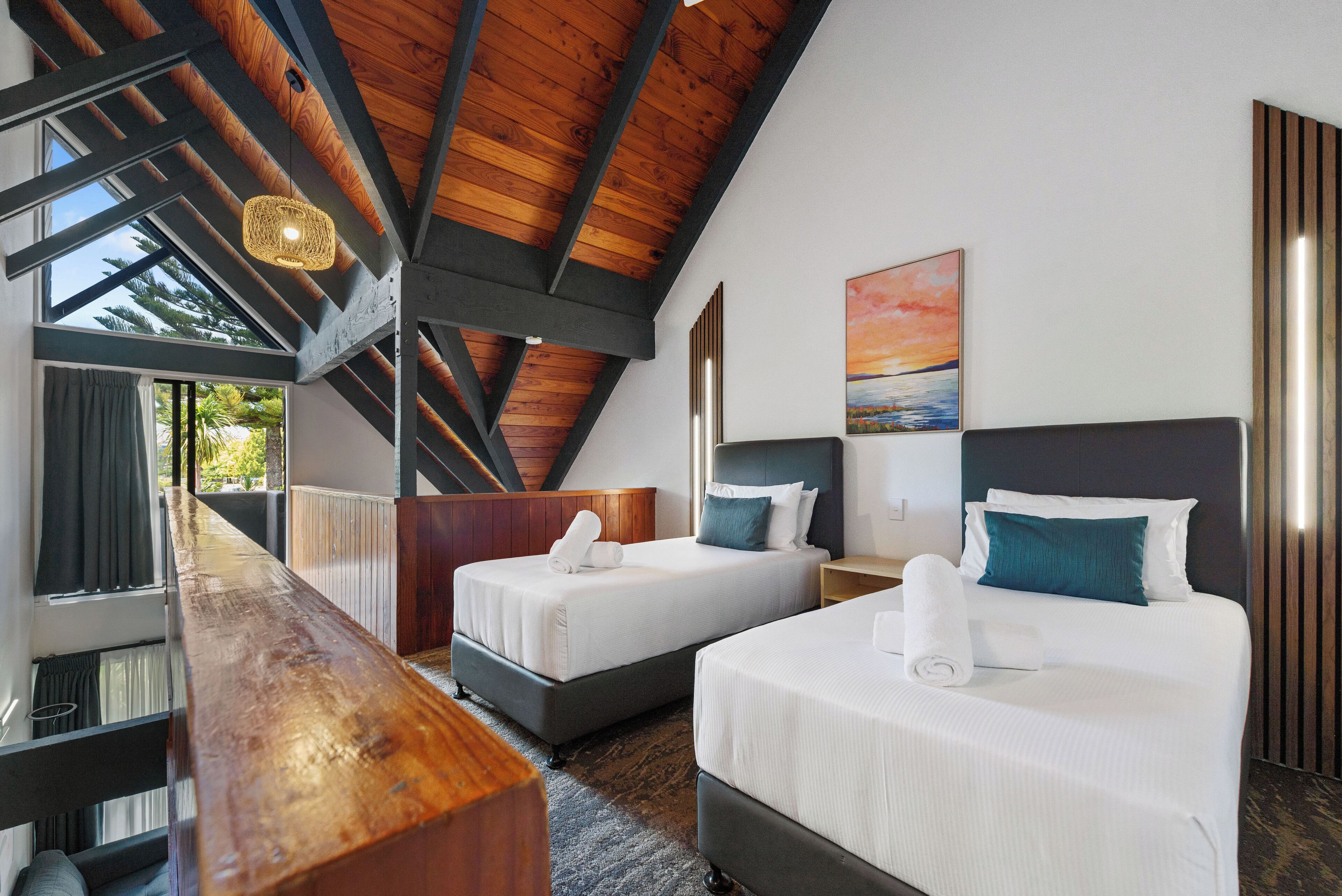 A hotel room with two beds, a wooden ceiling, a large window, and a painting on the wall.
