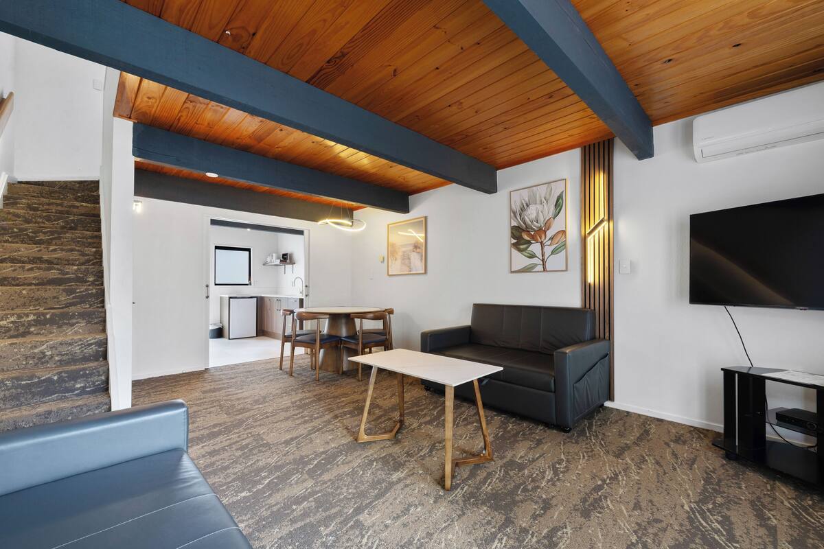 A modern living room with a wooden ceiling, a gray sofa, a coffee table, and a flat-screen TV.