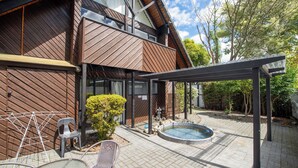 Uma casa moderna com fachada de madeira, um alpendre coberto, piscina e móveis de exterior.