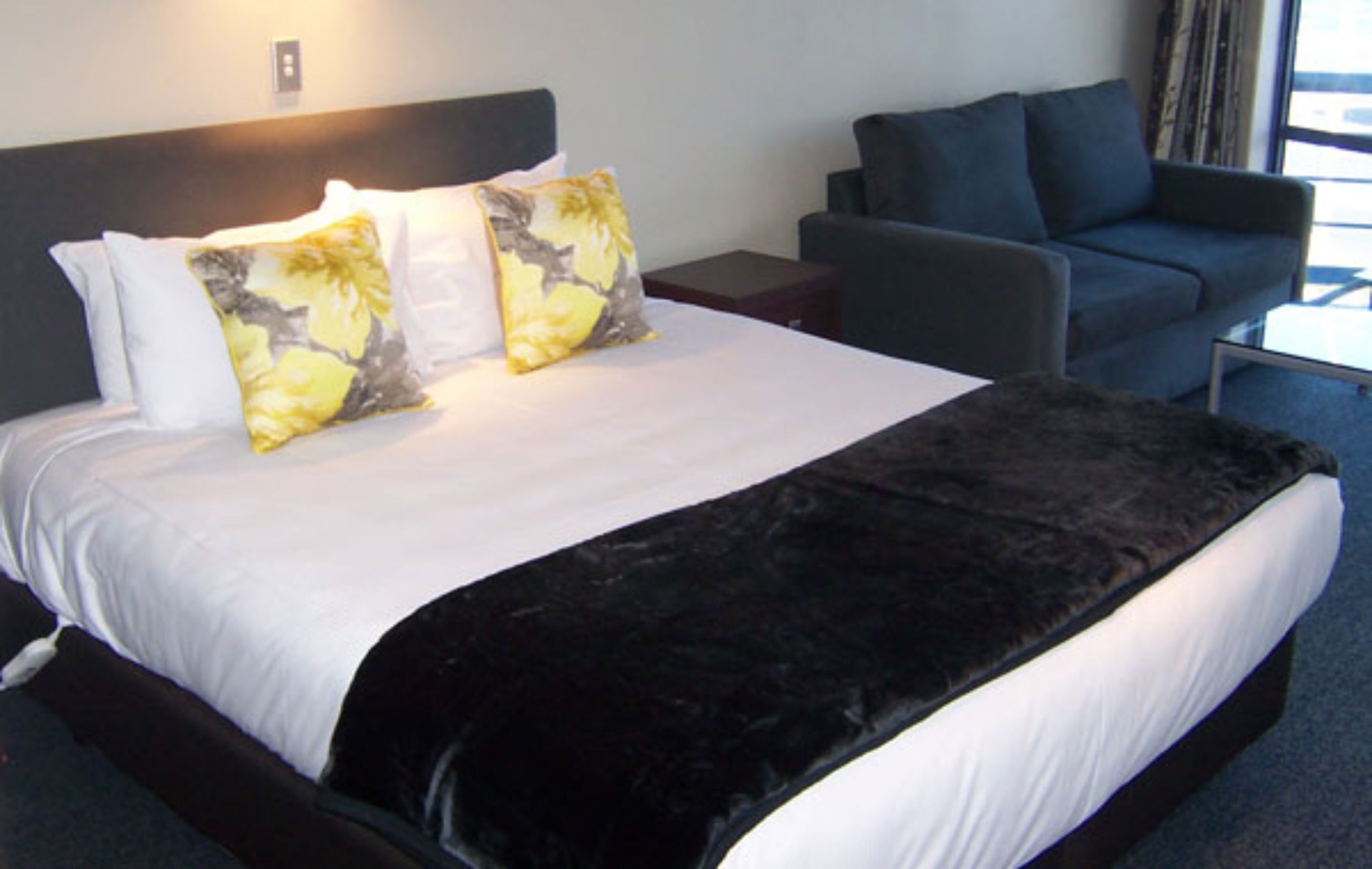 A hotel room with a large bed, a dark-colored sofa, and a small table.