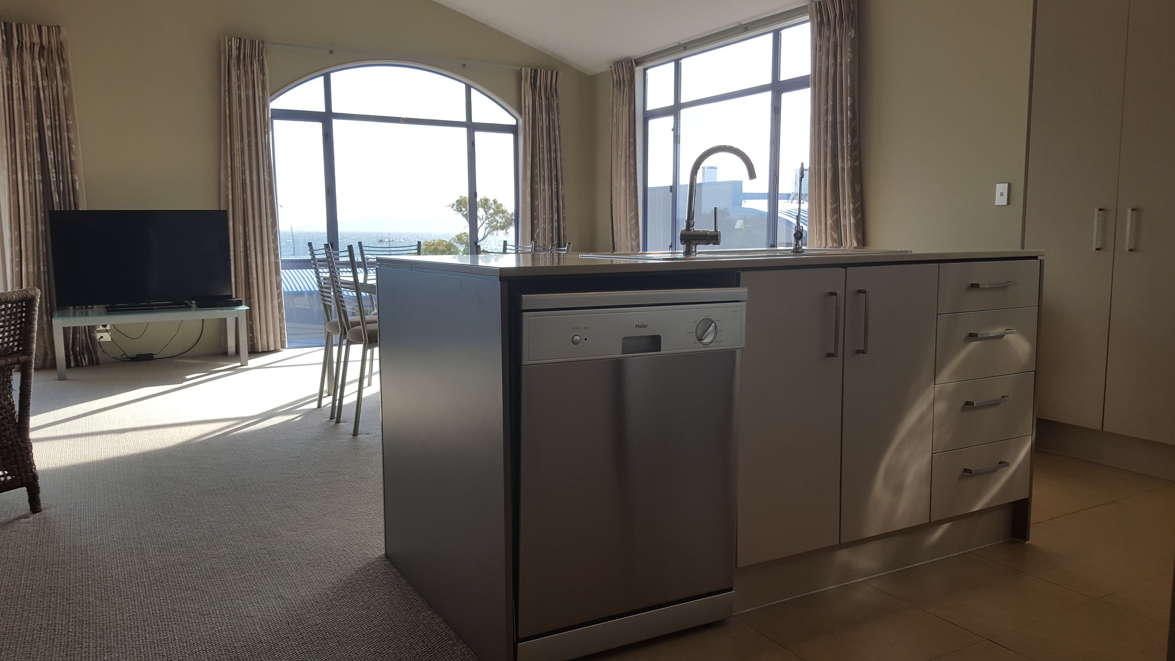A modern kitchen with a dishwasher, cabinets, and a dining area with a TV and chairs.