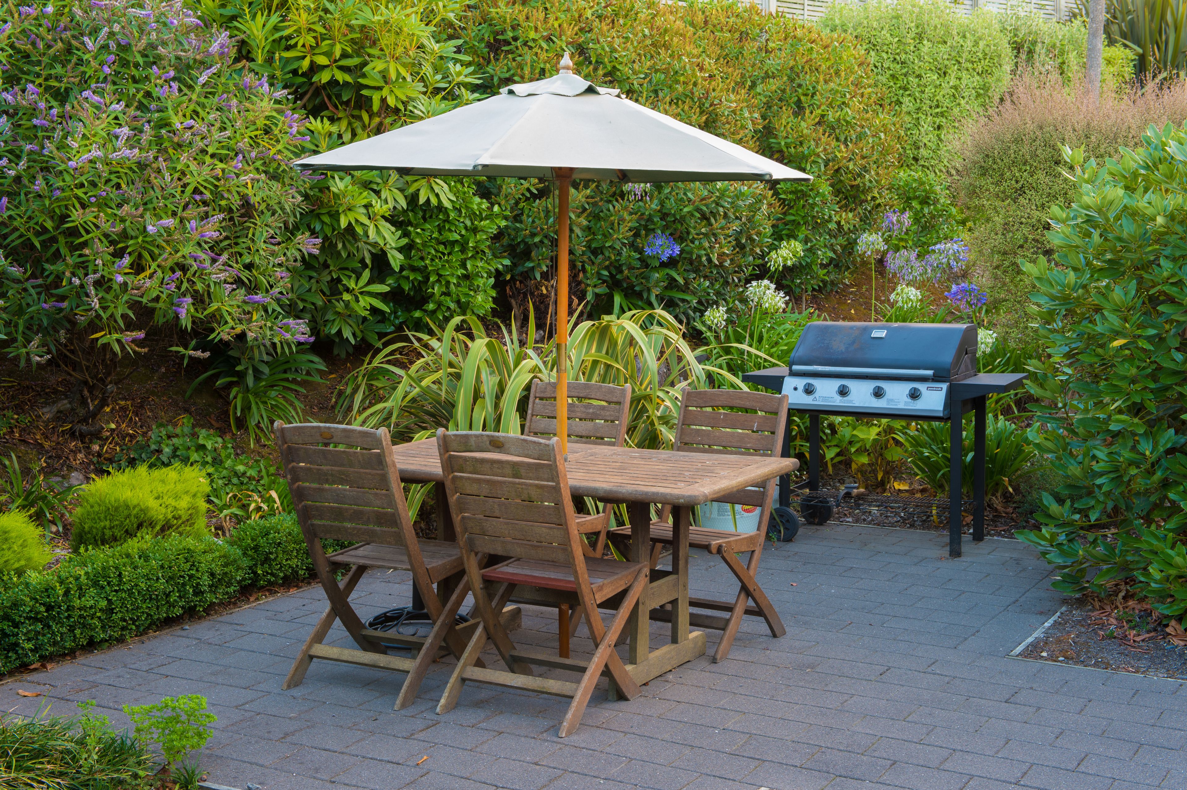 Un patio con una mesa y sillas de madera, una sombrilla y una parrilla.