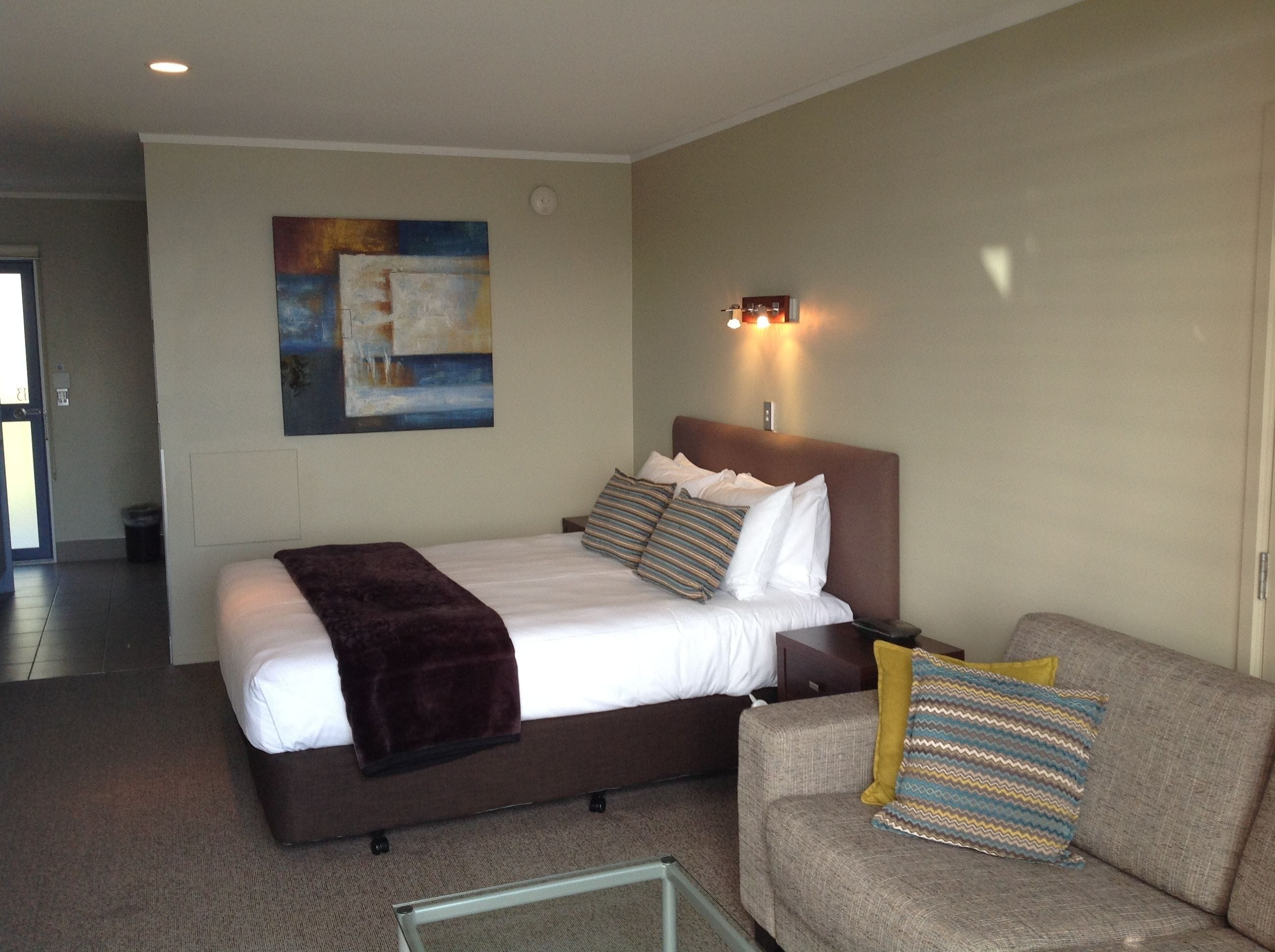 A hotel room with a bed, a couch, a painting on the wall, and a nightstand with a lamp.