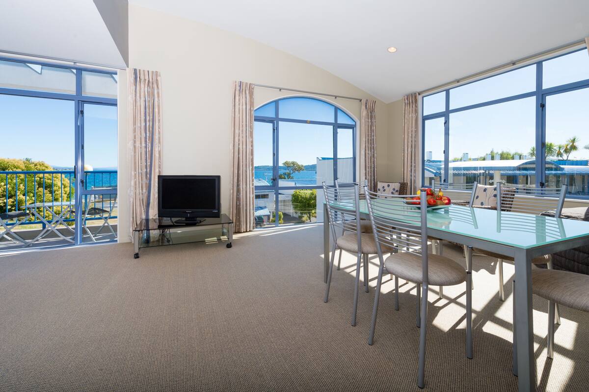 Une chambre d’hôtel moderne dotée d’un grand balcon, d’une table à manger en verre et d’un téléviseur à écran plat.