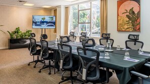 A conference room with a long table, black chairs, a TV screen, and large windows.