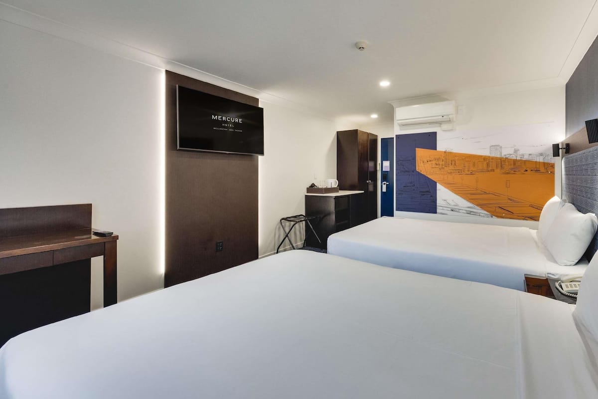 Ein Hotelzimmer mit einem Bett, einem Schreibtisch, einem Stuhl, einem Fernseher und einer Wand mit einem Stadtbild-Mural.