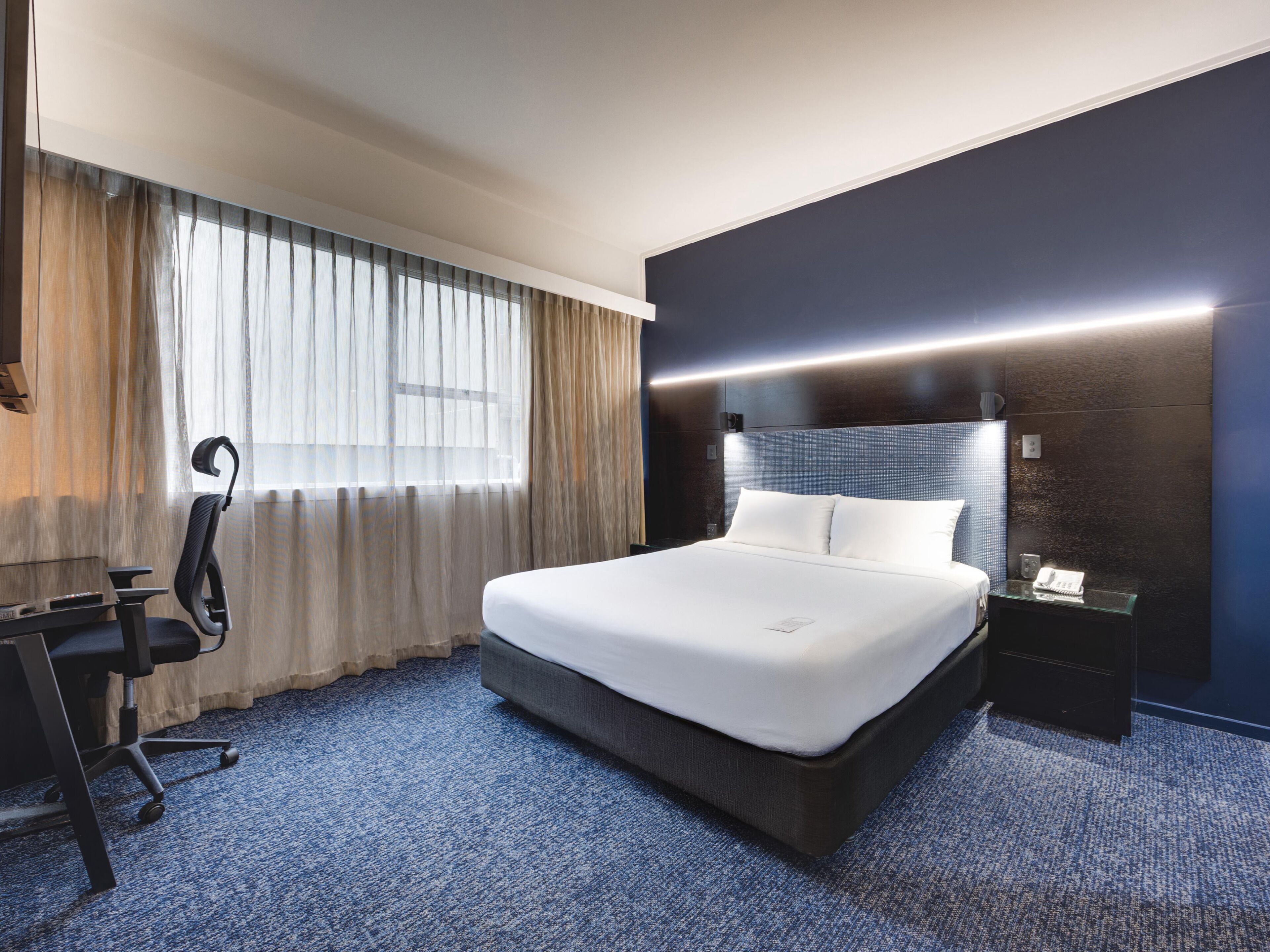 A modern hotel room with a large bed, a desk, and a chair.