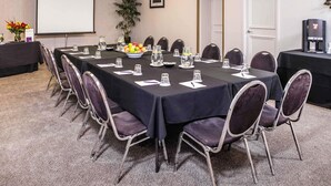 A conference room with a long table, chairs, a projector screen, a coffee machine, and a potted plant.
