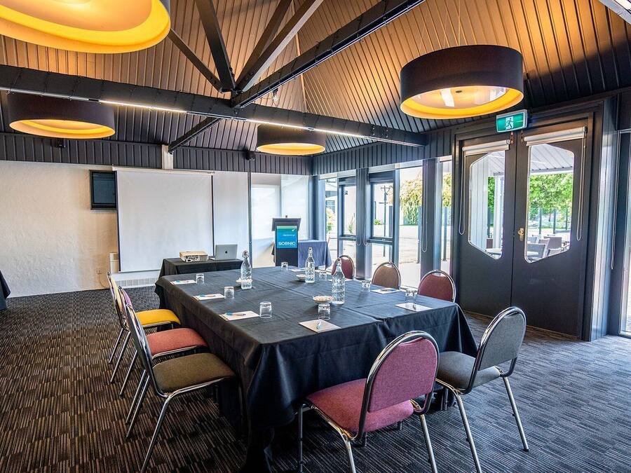 Een vergaderzaal met een lange tafel, stoelen, een projecter en een scherm.