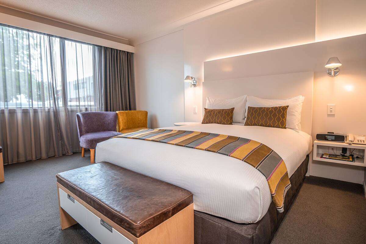 A hotel room with a bed, a chair, a bedside table, and a nightstand.