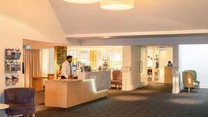 Un hall d'hôtel moderne avec un comptoir d'accueil, un espace salon et un bar/lounge en arrière-plan.